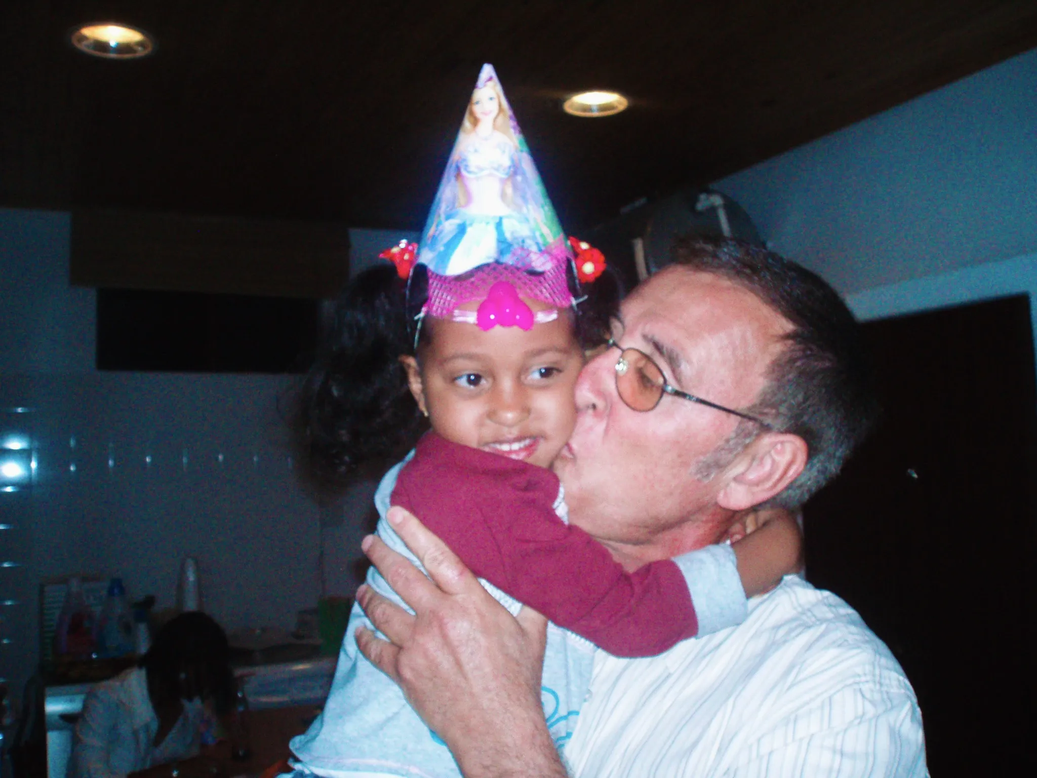 Rafaela as a little girl in a party hat, getting a kiss on the cheek